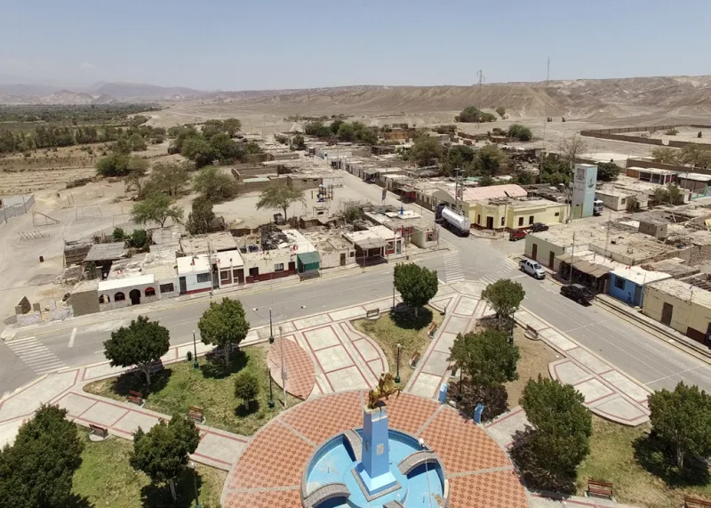 Vista elevada de una plaza con jardines, monumento central y viviendas alrededor.