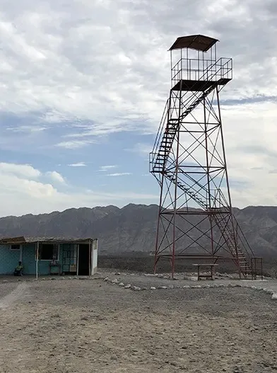 Torre metálica con escaleras, plataforma y techo sobre un terreno árido.